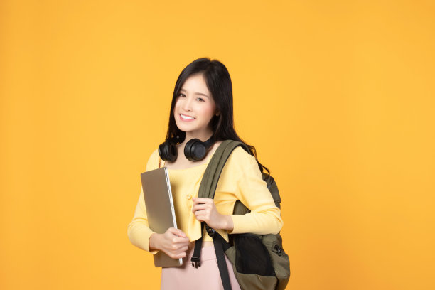 肖像快乐休闲的亚洲女生与背包，耳机和笔记本电脑孤立的黄色背景。回归学校和学习理念。图片下载