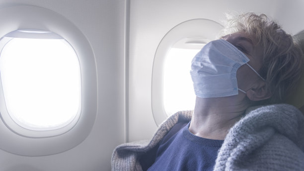 戴着面罩的成熟女性在飞机上睡觉。图片下载