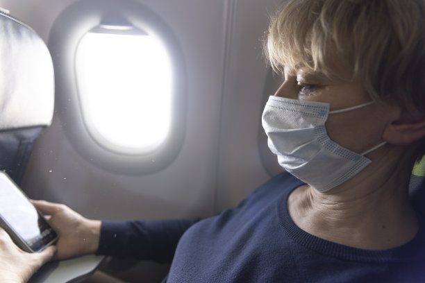 旅行期间大流行。高加索成熟女性坐在飞机上，用她的智能手机。图片下载