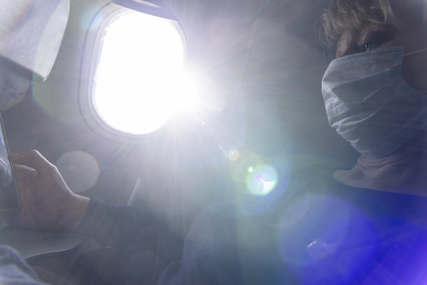 旅行期间大流行。高加索成熟女性坐在飞机上，用她的智能手机。阳光会产生强烈的透镜耀斑。图片下载