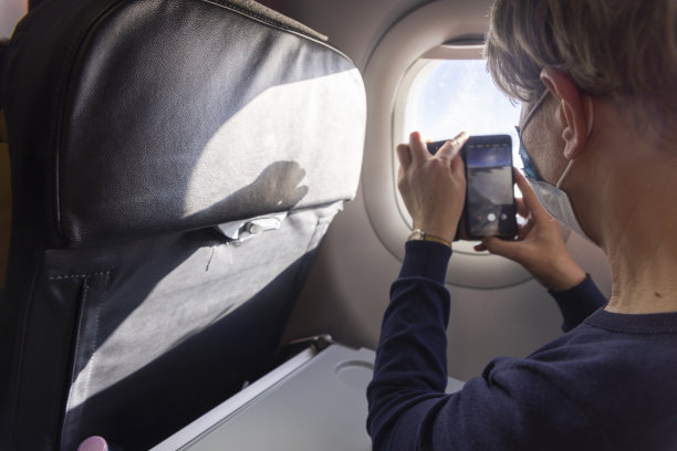 从飞机窗户拍摄视频。成熟女人在飞行过程中从窗口拍视频。图片下载