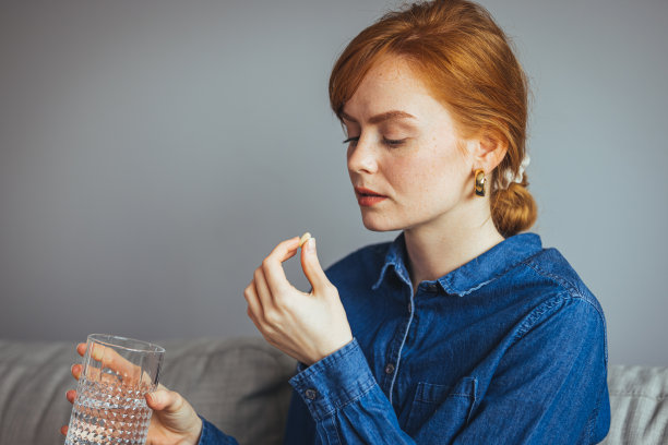 年轻漂亮的女人用一杯清水吃药片。图片下载