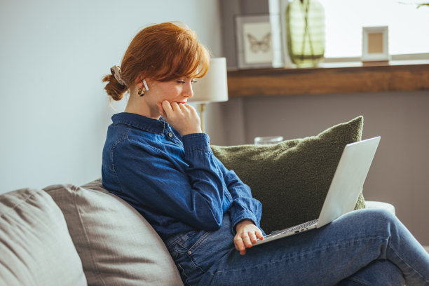 快乐的年轻女子坐在桌前，看着笔记本电脑屏幕，浏览，冲浪，无线互联网图片下载