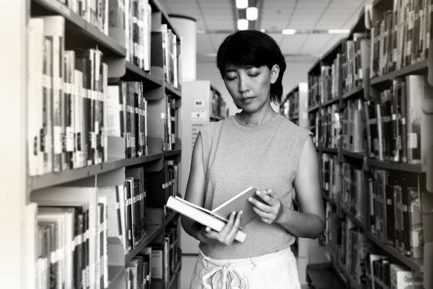 在图书馆里，迷离的书架旁，女人饶有兴趣地看书。图片下载