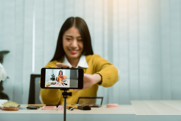 年轻的亚洲女性在家里用手机拍照，为自己的博客制作了一段关于化妆品的视频。图片下载