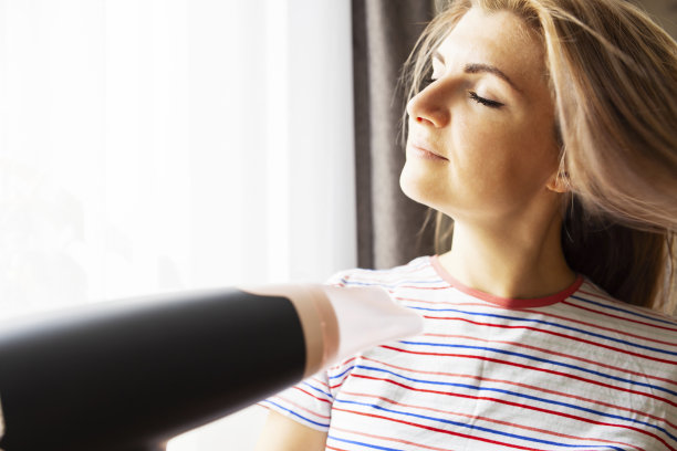 漂亮的年轻女子在家里靠窗用吹风机图片下载