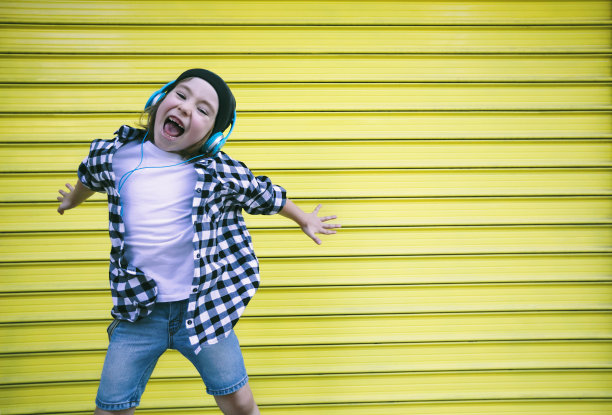 戴着耳机的快乐男孩在黄色的墙前蹦蹦跳跳图片下载