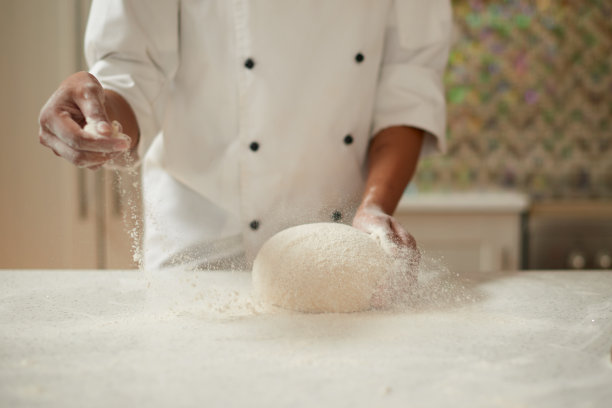 面包师在披萨面团上撒面粉。穿着围裙的厨师在凌乱的桌子上做面团。一位面目全非的厨师正在厨房桌子上准备披萨面团。图片下载