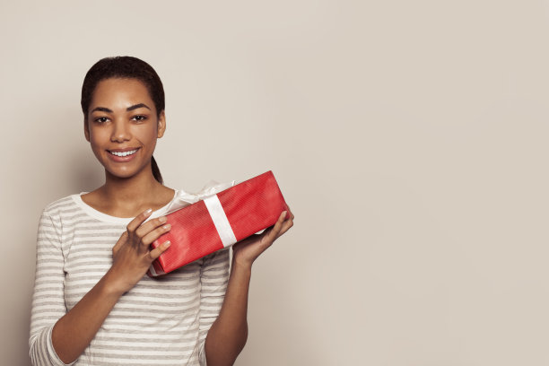 迷人的年轻黑人女子手持红色礼物礼盒白色丝带在白色背景图片下载