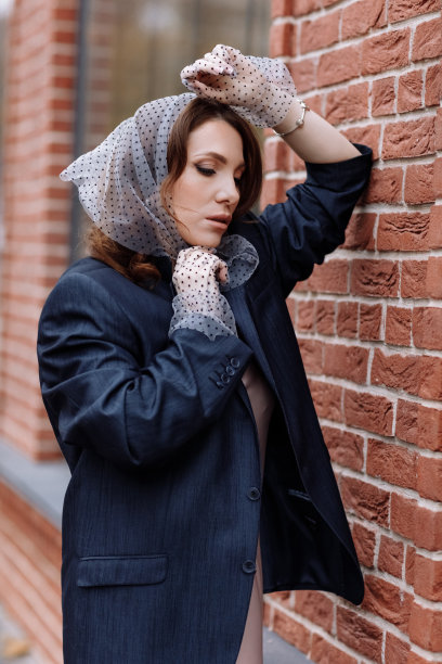 时尚年轻女性的肖像，发型，波尔卡圆点披肩和手套与化妆在外面摆姿势。一个穿着深色夹克的黑发女子出现在镜头前图片下载