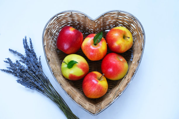 红苹果蓝莓和李子在草篮做成的心形在深蓝色的背景照片摄影图片
