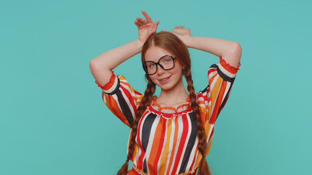 可爱有趣的红发女孩微笑友好，做兔子耳朵的手势在头上，有乐趣，愚弄图片下载