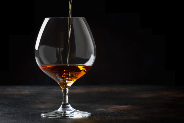 金色干邑倒进玻璃杯，复古棕色背景，图片下载