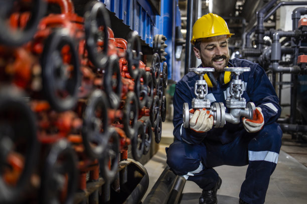 工厂工人手持崭新的工业高压阀门在生产厂。图片下载