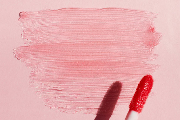 涂抹闪亮的唇彩和唇彩刷在粉红色的背景，硬阴影图片下载