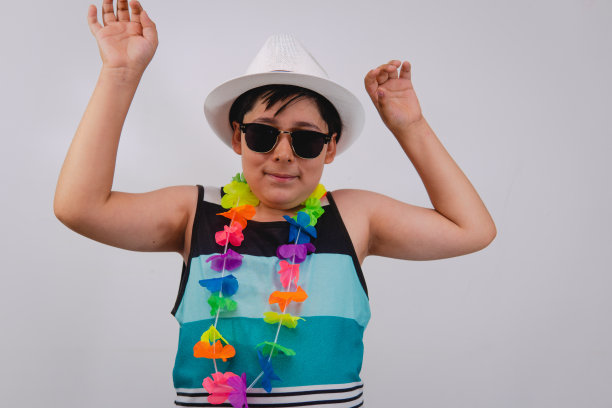 快乐的孩子穿着沙滩上的衣服在白色的背景和花项链。海滩上一个非常活泼的男孩，双臂高高举起。图片下载