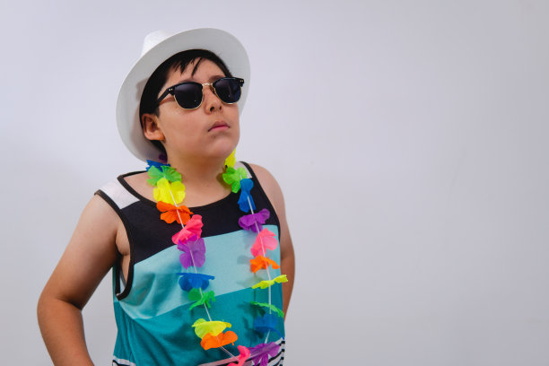 男孩在白色孤立的背景下，穿着沙滩服摆姿势。这个男孩穿着一件无袖衬衫，戴着一顶白色的帽子图片下载