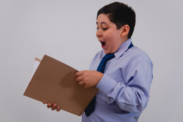 一个男孩穿着优雅的衬衫和领带假装成一个商人，一脸惊讶地看报纸。图片下载