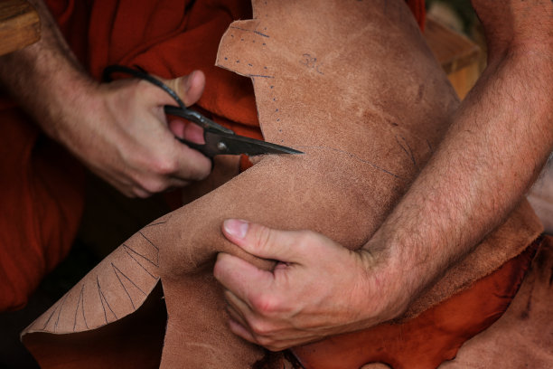 在中世纪的市场上，一名工匠用剪刀切割皮革，制作具有历史意义的鞋子图片下载