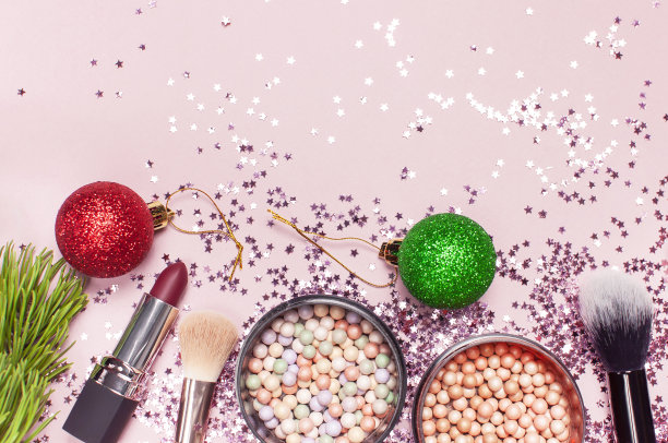 化妆刷，腮红粉，圣诞球，口红，全息闪光彩纸在粉红色背景上以星星的形式平铺俯视复制空间。化妆品配件,假期图片下载