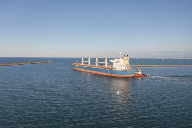 在海上拖着一艘大型货船的拖船。图片下载