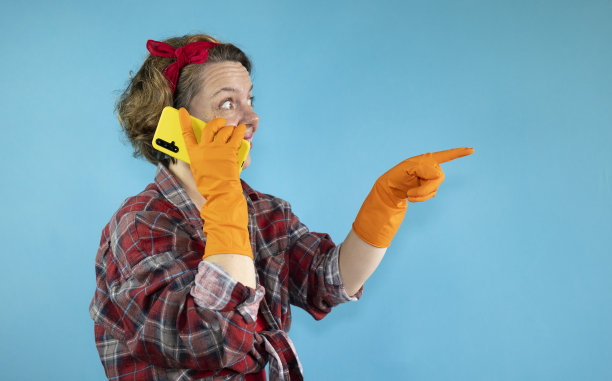 成年性感女郎穿着格子衬衫，在蓝色背景上戴着橙色清洁手套，正在打电话图片下载