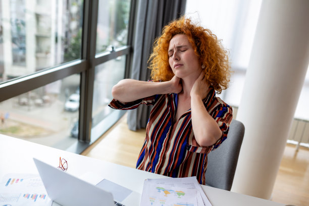 感觉筋疲力尽。沮丧的年轻女子看起来很疲惫，坐在她的工作地点按摩她的脖子图片下载