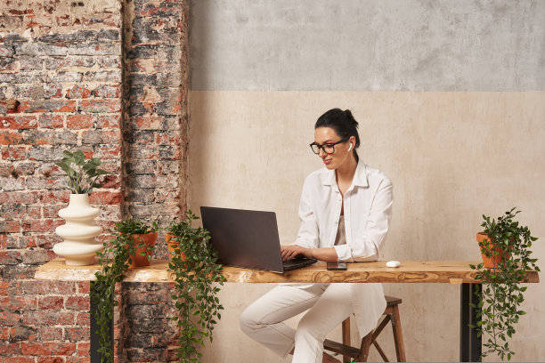 一个年轻美丽的女人带着大大的美丽的微笑在笔记本电脑前工作，手里拿着眼镜。家庭办公室。设计师,自由职业者图片下载