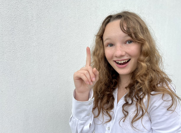 一个十几岁的女孩在白色背景上举起她的手指，她想到了什么或想起了什么，她很高兴，高兴有一个地方的文字图片下载