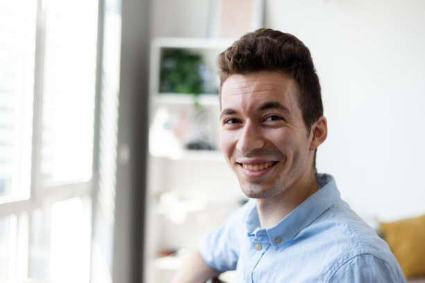 一个年轻快乐的男人的肖像，微笑着看着相机玩得很开心。男性在办公室在家工作的头像。图片下载