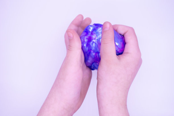 两种颜色的蓝色和粉色黏液在一个人的手在白色的背景。粘液被压碎、拉伸、撕裂和挤压图片下载