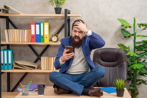 紧张的经理抓着头在手机里看短信，盘腿坐在桌子上，惊慌失措图片下载