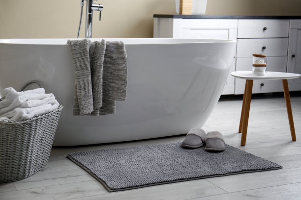 柔软的灰色垫子，地板上有拖鞋，靠近浴室的浴缸。室内设计图片下载