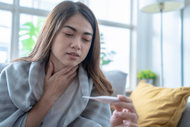 患有流感的亚洲妇女坐在家里客厅的沙发上。图片下载