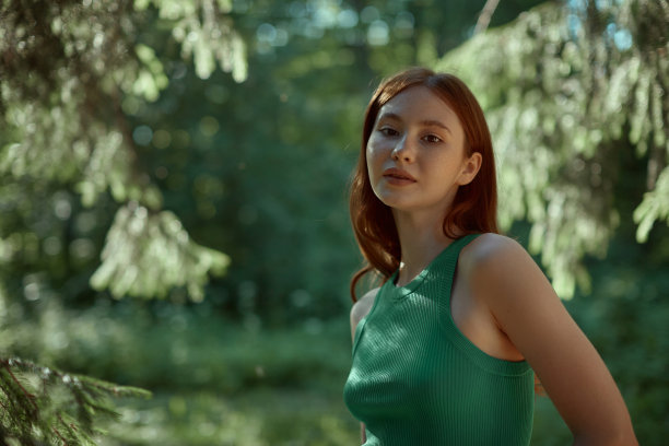 在树林里积极快乐的年轻女人的肖像。一个红发女孩的特写，绿色上衣上有雀斑。图片下载