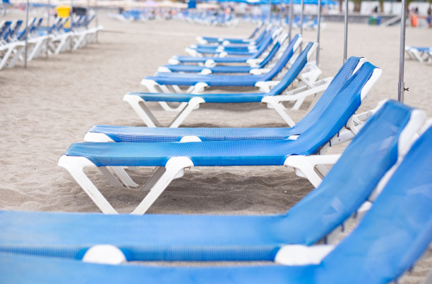 在一个多云的夏天，一排蓝色的空日光浴床和沙滩伞的透视视图图片下载