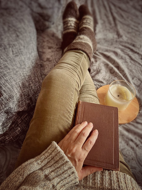 俯视图女人坐在床上穿着温暖的衣服，拿着一本书图片下载