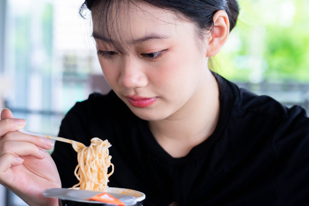 亚洲妇女在家里用塑料叉子吃面杯图片下载