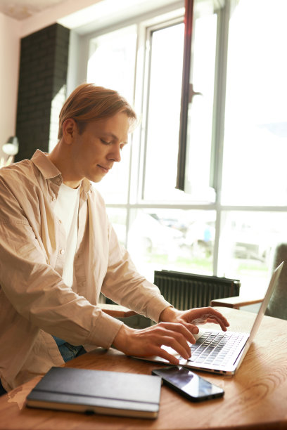 聪明的亚洲年轻男子一边在工作空间喝咖啡，一边用笔记本电脑工作。图片下载