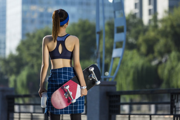年轻的东亚妇女的背影后，城市街头滑板-股票照片图片下载