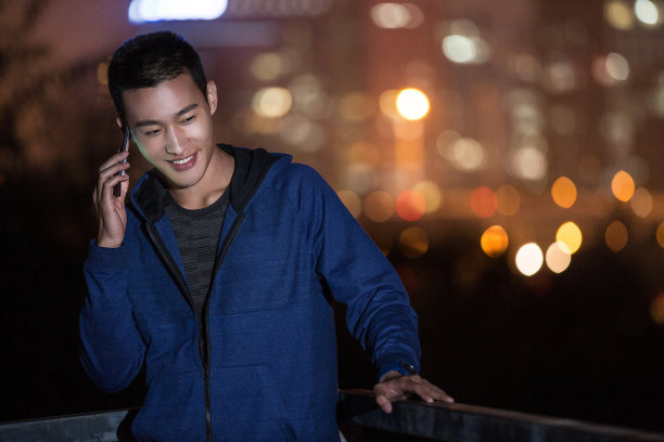 年轻的东亚男子使用手机在体育训练期间在城市街道在夜间-库存照片图片下载