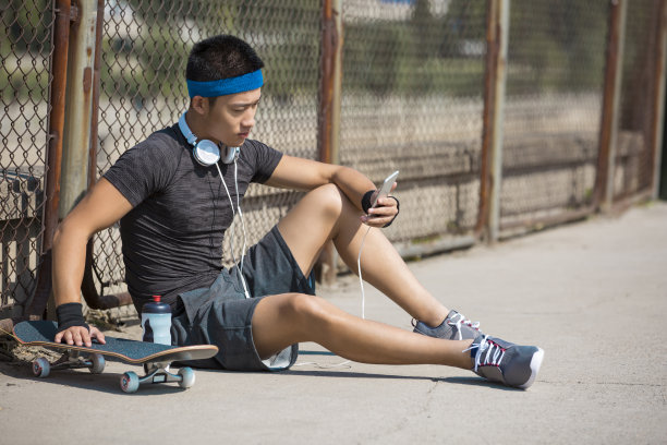 年轻的东亚男子休息后，滑板练习在城市体育综合体在一天的股票照片图片下载