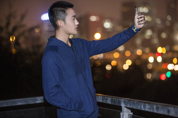 年轻的东亚男子使用手机在体育训练期间在城市街道在夜间-库存照片图片下载