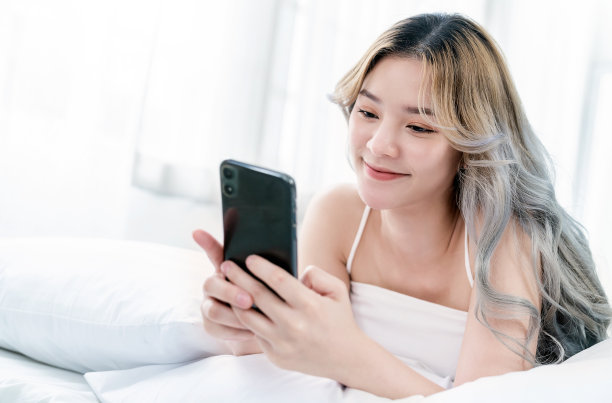 年轻美丽的亚洲女性肖像放松使用智能手机小工具在卧室。微笑快乐的亚洲女孩网上购物工作从家里。教育、电子商务、自由职业技术连接亚洲人素材图片
