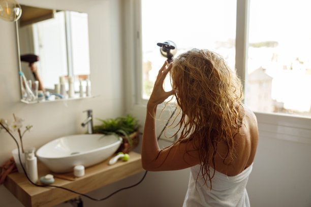 后方年轻的金发白种人妇女在毛巾干燥头发与烘干机在浴室。图片下载