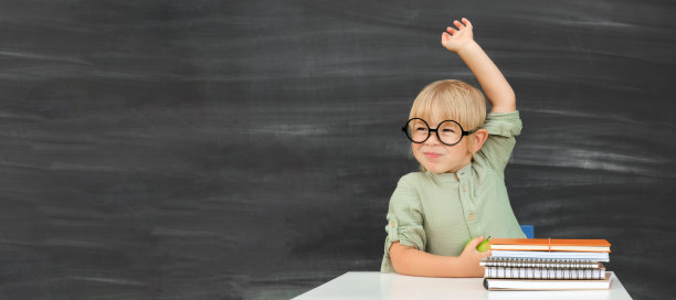 回到学校。快乐微笑的小学生戴着圆眼镜坐在课桌前。教室里有个孩子在黑板上举手。小男孩，上小学的。秋天的第一天。图片下载