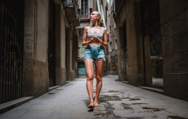 快乐的女游客手机用户走在老城小巷使用智能手机。GPS地图的概念。西班牙巴塞罗那。图片下载