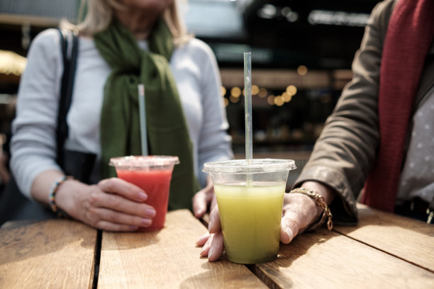 特写两个成熟的女人手拿果汁杯在桌子上。图片下载