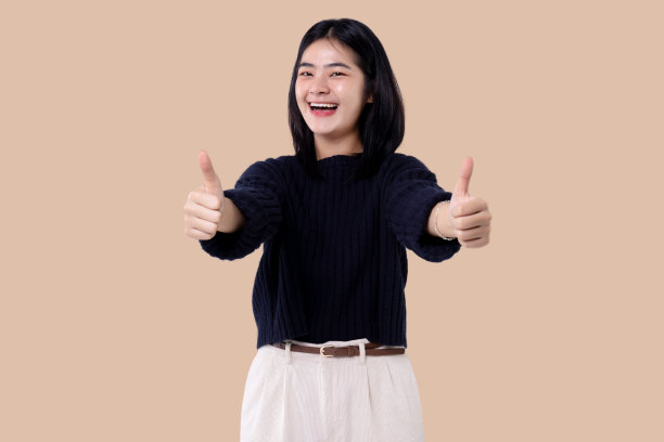 一个年轻的现代亚洲女性的肖像竖起大拇指，看着相机在孤立的背景。图片下载