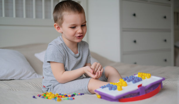 一个快乐的白人小男孩在一个明亮的房间的床上收集彩色马赛克创造图像图片下载